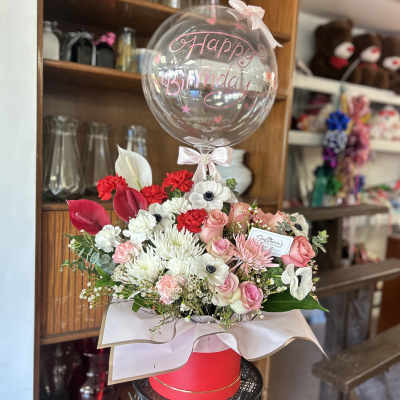 Birthday balloon over a mixed pink and white flower arrangement in a box