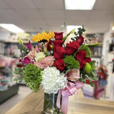 Mixed bouquet of red roses, white hydrangea, and yellow blooms in a glass vase
