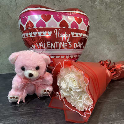 Pink teddy bear, heart balloon, and white rose bouquet on a table