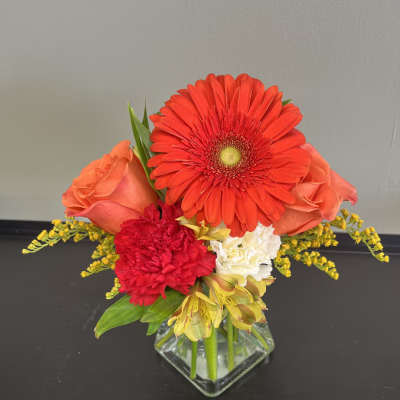 Bright mixed bouquet in a square glass vase with red and orange blooms