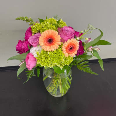 Mixed pink and peach flowers arranged in a clear glass vase