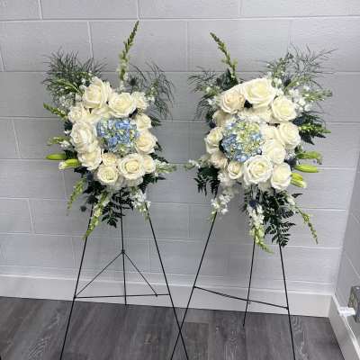 Two white rose and blue hydrangea standing floral sprays on black easels