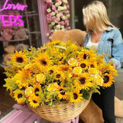 Large basket of sunflowers and yellow roses held by a woman
