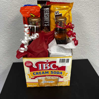Gift basket with candy bars and two small soda bottles in a cream soda box