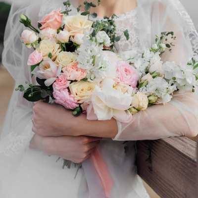 Bride holding a pastel bouquet of roses, ranunculus, and white blossoms