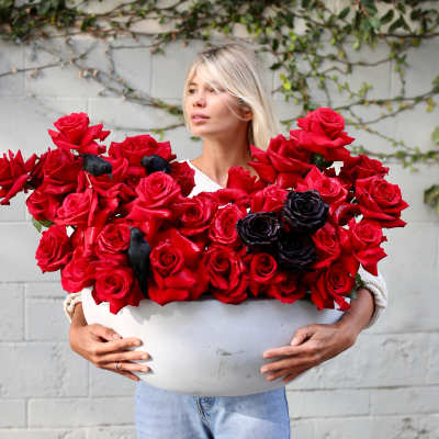 Woman holding a large white bowl of red roses with a few black roses