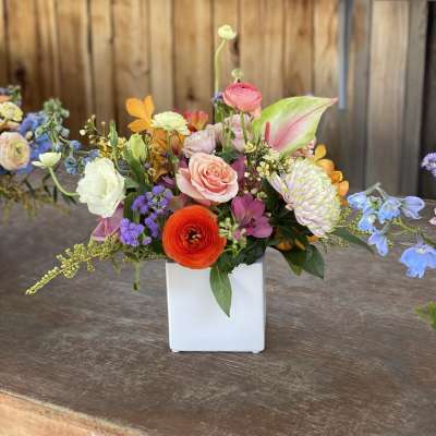 Colorful mixed flower arrangement in a white square vase