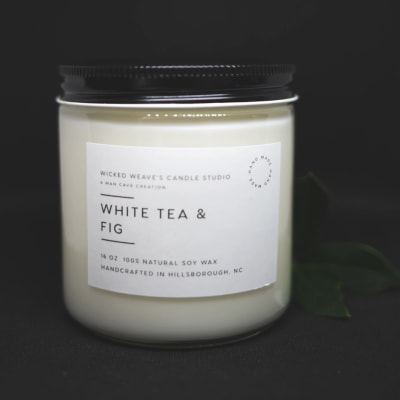White candle in a glass jar with a black lid and label