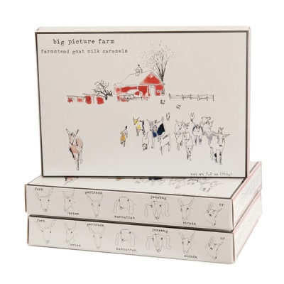 Stacked boxes of farmstead goat milk caramels with illustrated goats and a red barn