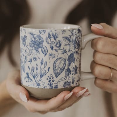 Hands holding a blue floral-patterned ceramic mug
