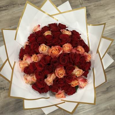 Bouquet of red and peach roses wrapped in white paper with gold trim