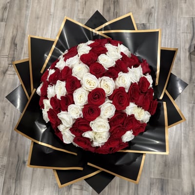 Round bouquet of red and white roses wrapped in black paper with gold trim