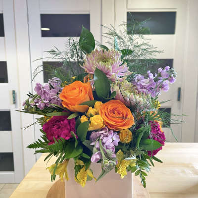 Mixed bouquet in a white square vase with orange and purple flowers