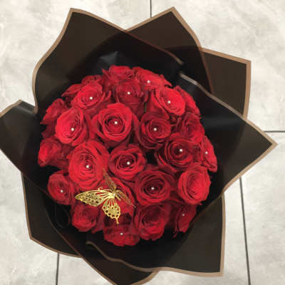 Bouquet of red roses wrapped in black paper with a gold butterfly accent