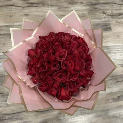 A bouquet of red roses wrapped in pink paper with gold trim.