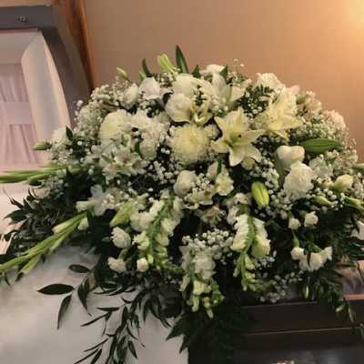 Large white funeral casket spray with lilies and baby’s breath