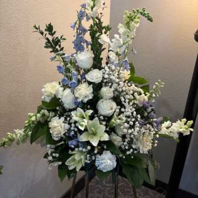 Tall white and blue floral funeral spray on a stand