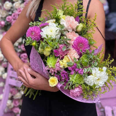 Woman holding a mixed bouquet of pink, white, and yellow flowers
