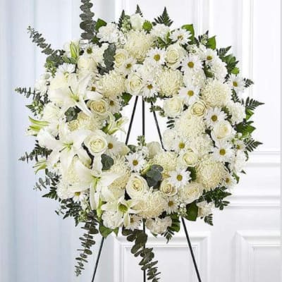 White floral wreath on a black stand with roses and daisies