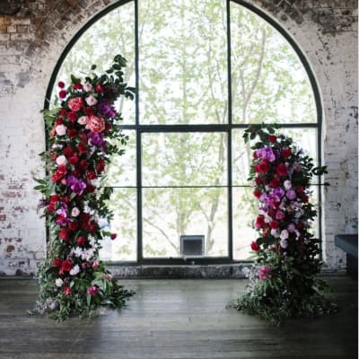 Two tall floral pillars with red, pink, and purple blooms by a large window