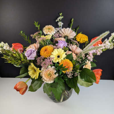 Mixed bouquet in a glass vase with orange tulips and pastel daisies