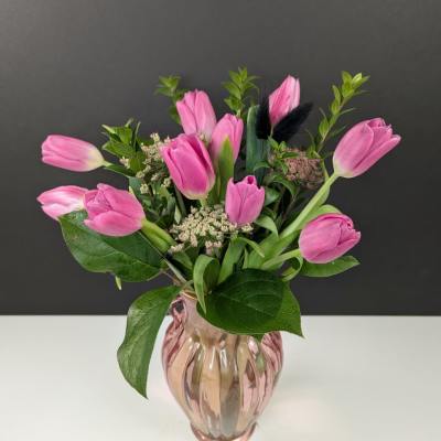 Pink tulip arrangement with small filler flowers in a pink glass vase