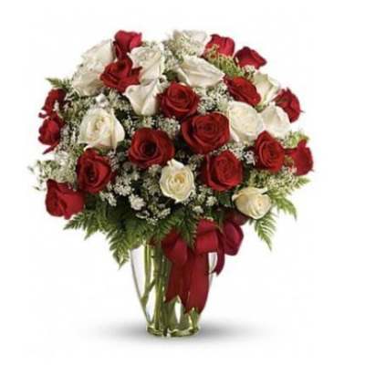 Arrangement of red and white roses with small white filler flowers in a clear glass vase with a red bow.