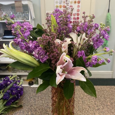 Pink lilies and purple flowers arranged in a tall glass vase