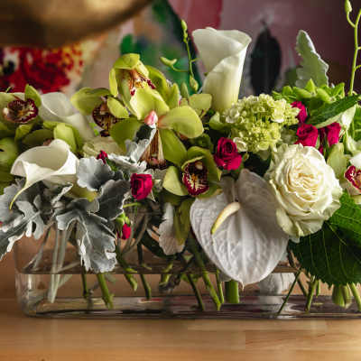 Mixed floral arrangement in a glass vase with white calla lilies, roses, and orchids