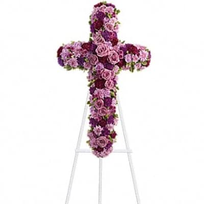 Cross-shaped floral tribute in pink and purple flowers on a stand