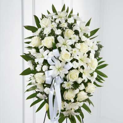 White floral standing spray with roses and lilies on a black easel