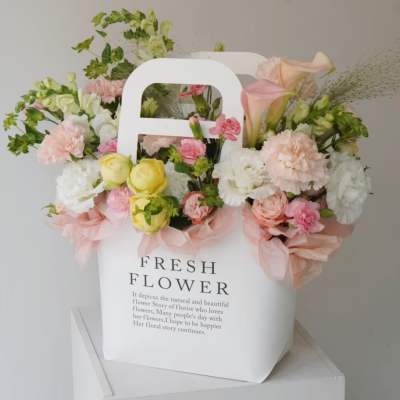 Pastel flower arrangement in a white gift bag with pink ribbon
