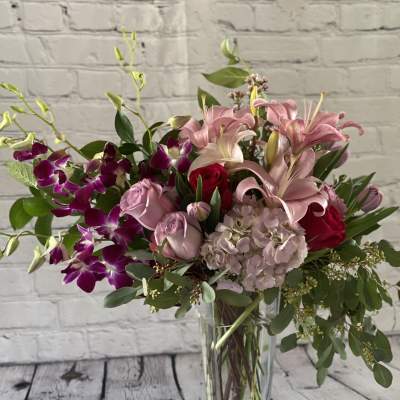 Pink lilies and roses in a clear glass vase with purple orchids