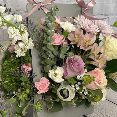 Mixed pastel flower arrangement in a gray gift box with pink ribbons