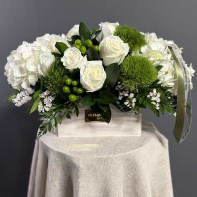 Low white arrangement of roses, hydrangeas, and green dianthus in a rectangular wooden box.