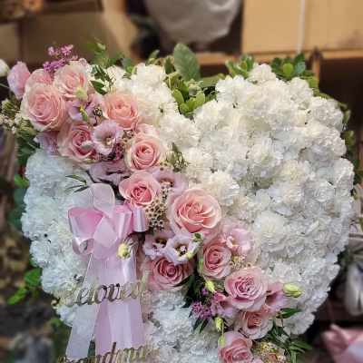 Heart-shaped floral arrangement with pink roses and white blooms, finished with pink ribbons