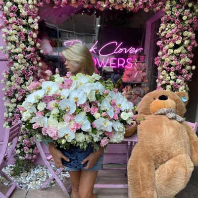 Woman holding a large bouquet of white orchids and pink roses beside a teddy bear