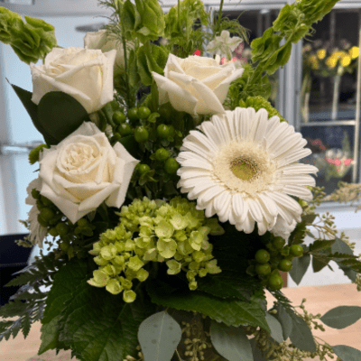 White roses, a white gerbera daisy, and green hydrangea arranged in a clear glass vase.