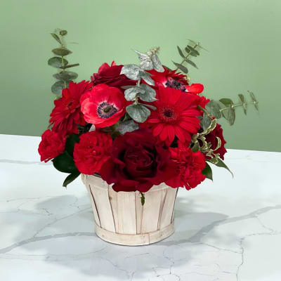 Red flowers arranged in a white wooden basket with silver eucalyptus