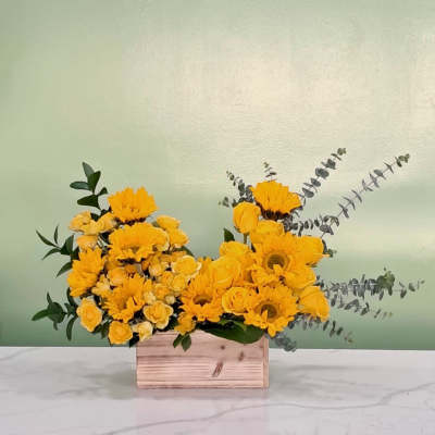 Yellow flowers arranged in a wooden box with eucalyptus accents