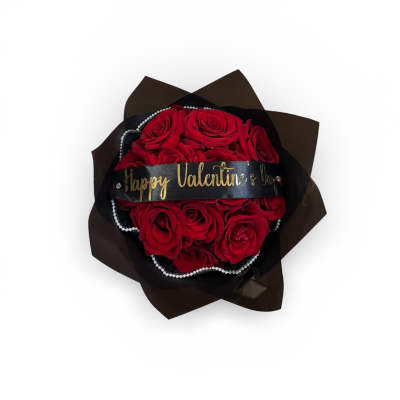 Round bouquet of red roses wrapped in black paper with a Happy Valentine’s Day ribbon and pearl accents.
