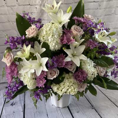 Large bouquet of white lilies, pink roses, and purple flowers in a white vase