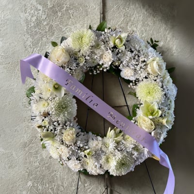 White floral wreath on a stand with a lavender ribbon