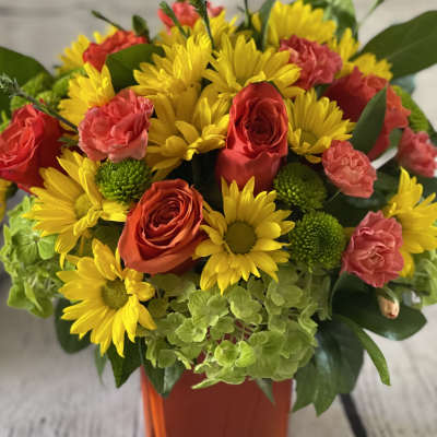 Bouquet of yellow daisies, red roses, and pink carnations in an orange vase