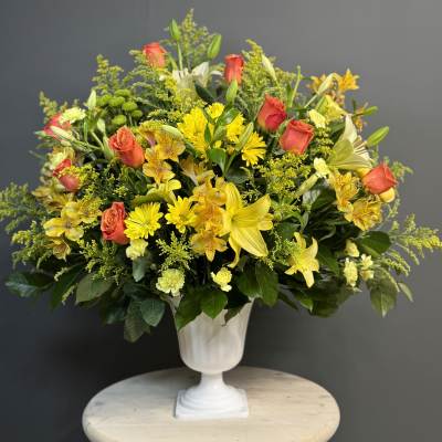 Yellow and coral mixed flower arrangement in a white pedestal vase