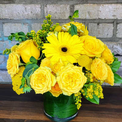 Yellow roses and a gerbera daisy in a green glass vase