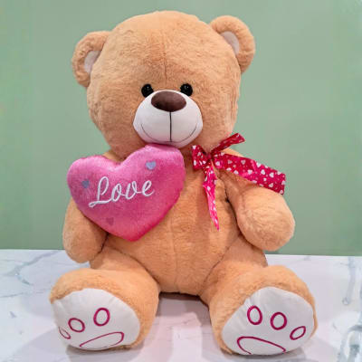 Plush teddy bear holding a pink heart with the word Love