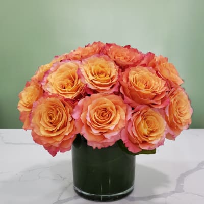 Orange and pink roses arranged in a dark glass vase