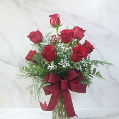 Red roses arranged in a glass vase with a burgundy ribbon
