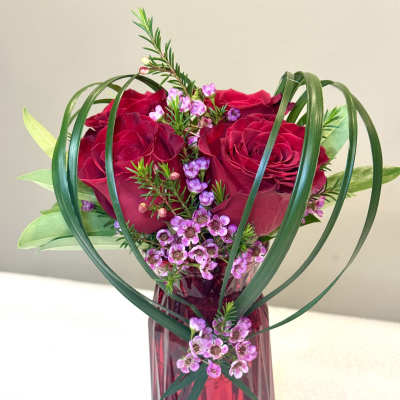 Red roses and pink filler flowers in a red glass vase